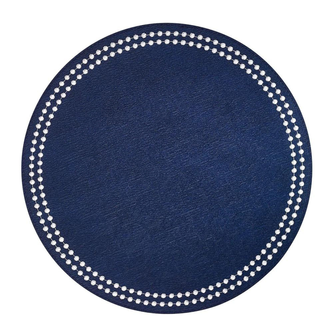 The Bodrum Pearls Round Placemat Set of 4 in dark blue is made from phthalate-free vinyl, featuring a textured surface and a circle of small white dots near the edge.