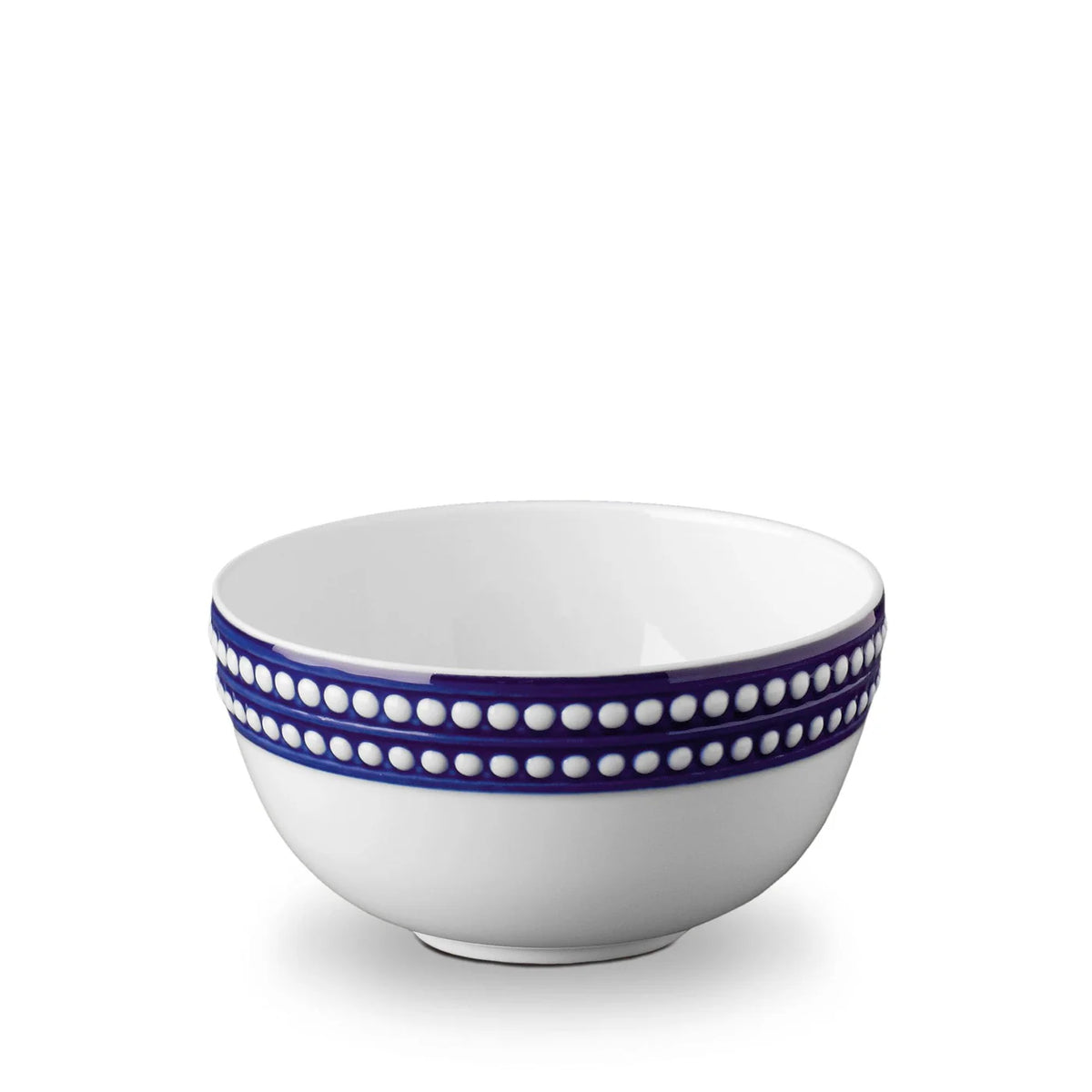 The L'Objet Perlèe Blue Dinnerware features a white ceramic bowl with two blue bands and raised white dots around the rim, reflecting classic blue and white style.