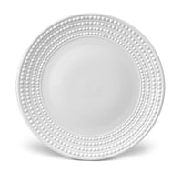 The Perlèe White Dinnerware by L'Objet features a round white Limoges porcelain charger plate with raised dot concentric circles on the rim and a smooth, plain center.