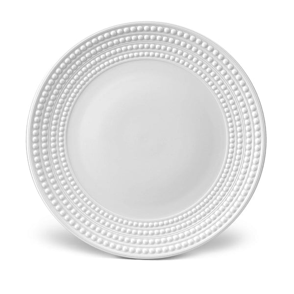 The Perlèe White Dinnerware by L'Objet features a round white Limoges porcelain charger plate with raised dot concentric circles on the rim and a smooth, plain center.