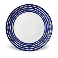 The L'Objet Perlèe Blue Dinnerware features a round ceramic plate with a white center and wide dark blue rim, accented by rows of evenly spaced white dots—ideal for fans of blue and white tableware.