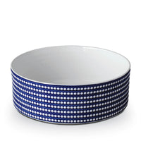 The L'Objet Perlèe Blue Dinnerware is a round white Limoges porcelain bowl with a dark blue exterior accented by rows of white dots. This smooth, handleless piece is part of the Perlèe collection.