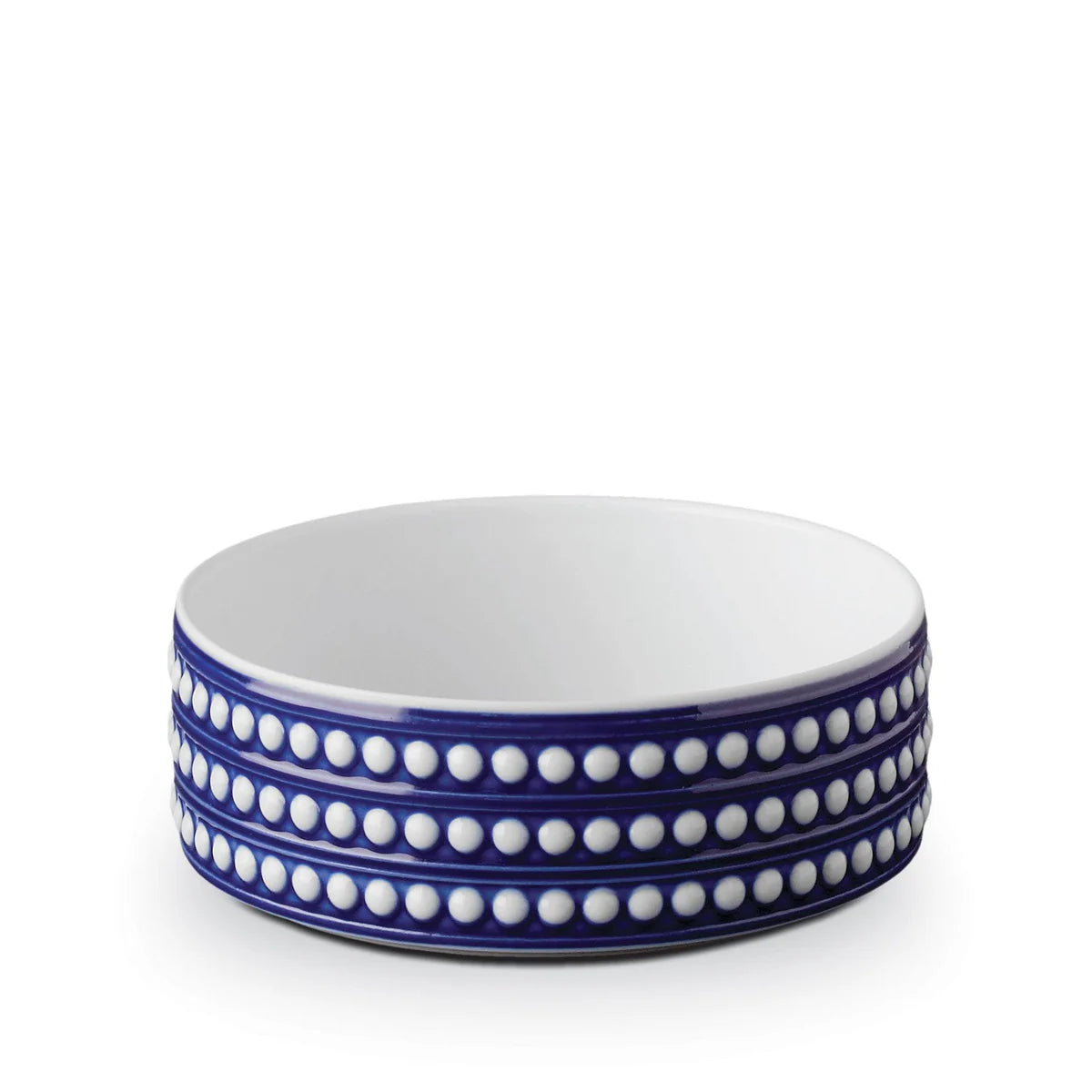 The Perlèe Blue Dinnerware bowl by L'Objet features a white interior, blue exterior, and three rows of raised white dots around the sides, echoing classic blue and white dinnerware. The bowl is shown against a plain white background.
