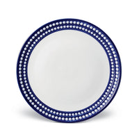 The Perlèe Blue Dinnerware by L'Objet is a round ceramic plate featuring a white center and a dark blue border adorned with two rows of raised white dots, reflecting timeless blue and white dinnerware design.