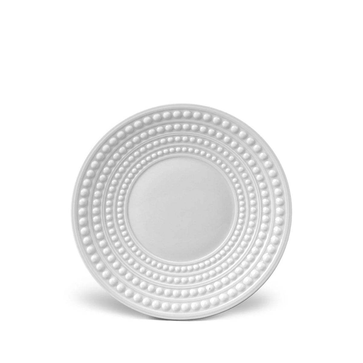 The Perlèe White Dinnerware charger plate by L'Objet features concentric raised dot patterns around the rim, crafted in white ceramic for an elegant, minimalist look.