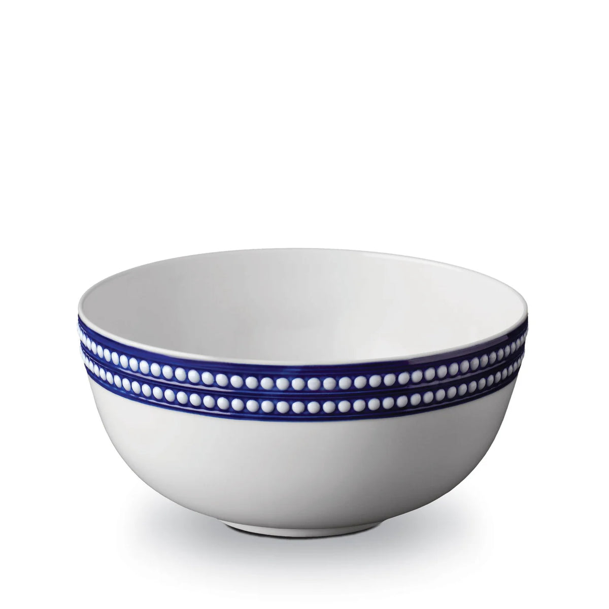 The Perlèe Blue Dinnerware by L'Objet features a white ceramic bowl with double rows of raised white dots on a blue rim, echoing classic blue and white dinnerware, displayed against a plain white background.