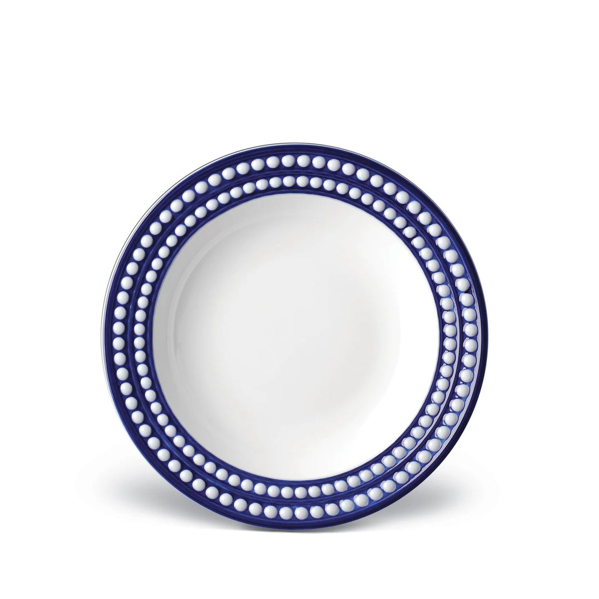 The L'Objet Perlée Blue Dinnerware features a round white plate with a glossy center and a wide, dark blue rim accented by two rows of white dots—ideal for fans of elegant blue and white table settings.