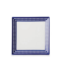 The Perlèe Blue Dinnerware by L’Objet is a square Limoges porcelain plate with a white center and a blue border accented by white dots—an elegant, modern choice for fans of blue and white dinnerware.