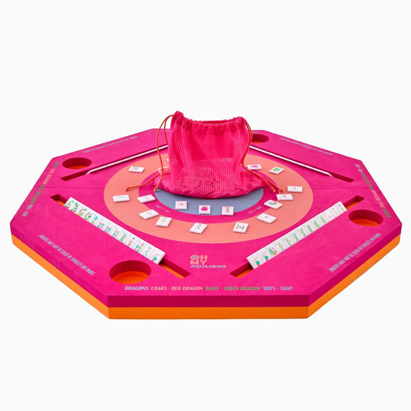 The Mahjong Aqua Pool Mat by Oh My Mahjong is an octagonal pink and orange set with tile racks, holders, a center tile area, red drawstring bag of tiles—ideal for gaming anywhere on this portable mat.