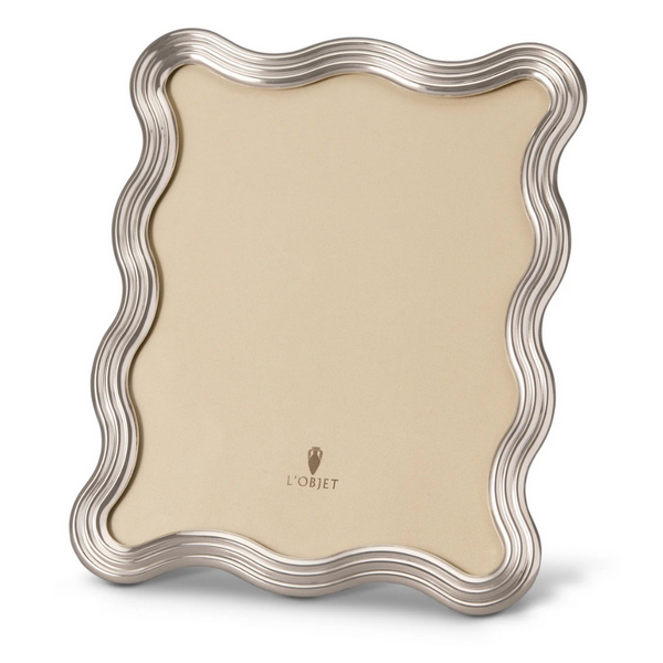 The L'Objet Ripple Frame Platinum features a wavy platinum-toned border, a beige center, and the L'Objet logo near the bottom. This modernist decorative frame stands upright against a plain white background.