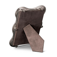 The Ripple Frame Platinum by L'Objet is pictured from the back, standing upright with a brown, suede-like support stand and backing, and features a scalloped platinum edge.