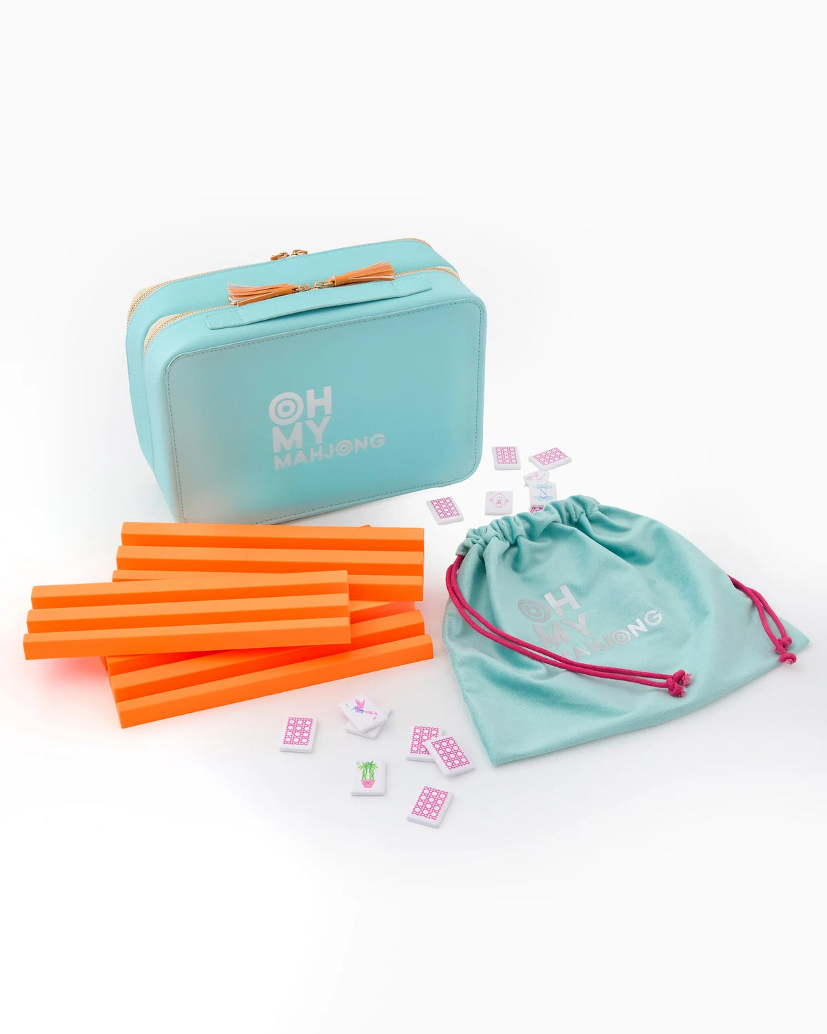 The Mahjong Debutante Travel Tile Set by Oh My Mahjong features a turquoise carrying case, orange racks, scattered tiles, and a turquoise drawstring pouch with pink strings, all displayed on a white background.