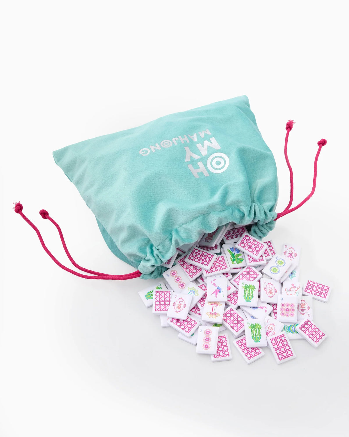 The Mahjong Debutante Travel Tile Set by Oh My Mahjong features a teal drawstring bag with pink cords, revealing colorful patterned tiles—perfect for introducing mahjong to kids anywhere.
