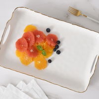 The PAMPA BAY Portofino Handle Rectangle Tray with a gold border displays sliced oranges, grapefruit, blueberries, and mint. Nearby on the marble surface are a gold fork and folded white napkins.