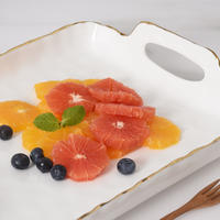 Slices of grapefruit and orange with fresh mint leaves and blueberries are arranged on the PAMPA BAY Portofino Handle Rectangle Tray, shown alongside a small wooden fork.