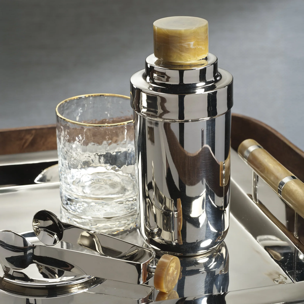 The Zodax Spector Cocktail Shaker in Nickel & Amber sits on a tray with a gold-rimmed tumbler and metal ice tongs, making the perfect set to elevate your mixology experience.
