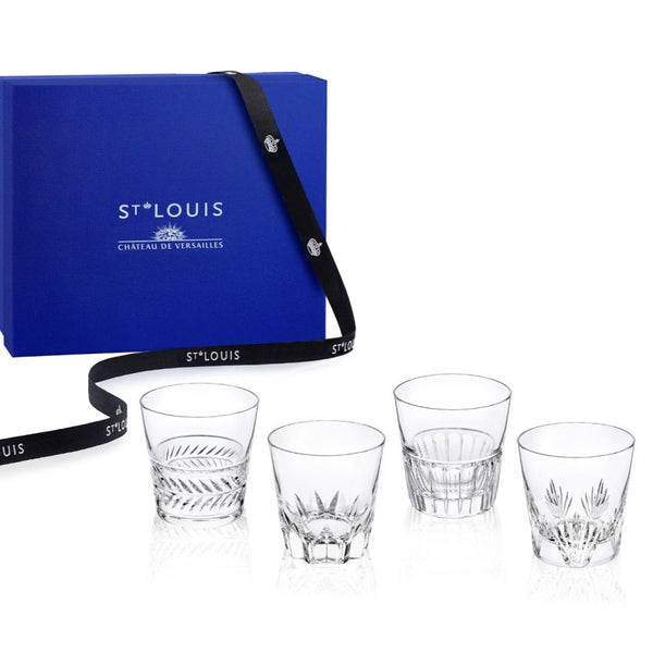 A blue Saint-Louis/Hermes Château de Versailles gift box with a black ribbon stands behind four clear Kings Hall Tumblers, each intricately cut in a unique design.