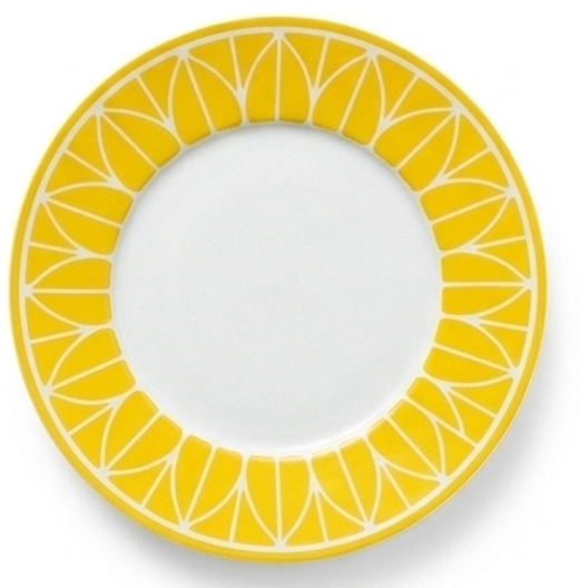 The Christofle Malmaison Riviera Dinnerware features a white plate with a bright yellow geometric rim, echoing lemon slices. Its plain center evokes elegant French Riviera dining.