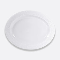 The Bernardaud Louvre Dinnerware features a plain white oval ceramic plate with a subtle decorative rim pattern inspired by Renaissance elegance, shown against a light gray background.