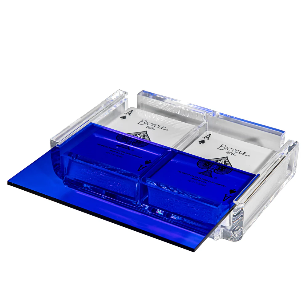 The La Pinta Card Deck Transparent by Luxe Dominoes features a clear blue acrylic box with a sliding lid, holding two decks of cards each showing an Ace of Spades on top. The lid is partially open, revealing the cards inside.