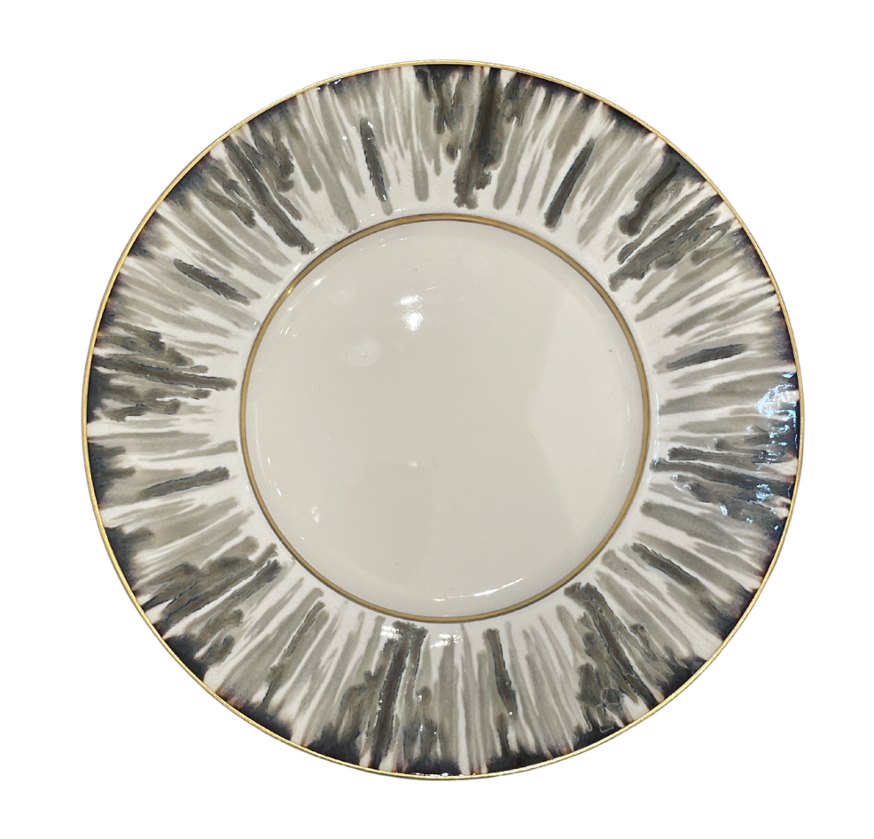 The JL Coquet Ecaille Creme Dinnerware features a round ceramic plate with a white center, a rim adorned with gray and black brushstroke patterns, contemporary accents, and a slim gold border.