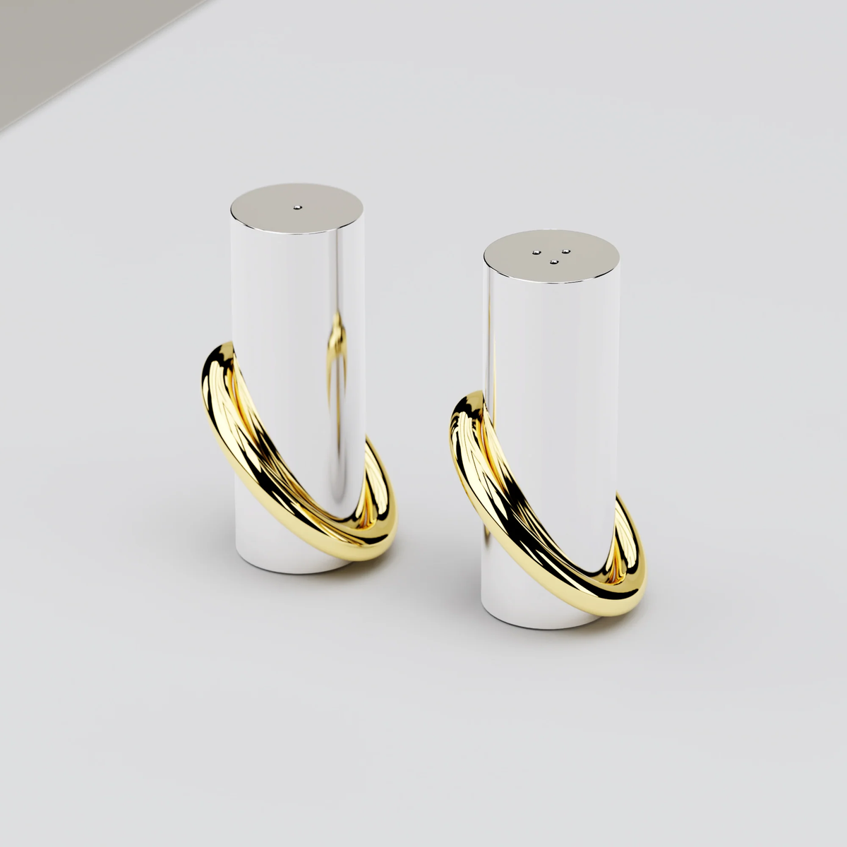The Anna New York Ring Salt & Pepper Shaker Set features two modern cylindrical shakers with shiny stainless steel finishes and brass gold rings at the base, displayed on a light-colored surface.