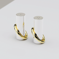 The Anna New York Ring Salt & Pepper Shaker Set features two modern cylindrical shakers with shiny stainless steel finishes and brass gold rings at the base, displayed on a light-colored surface.