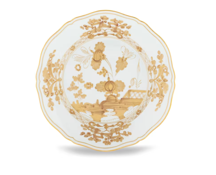 The Oriente Italiano Aurum plate by Ginori 1735 is crafted from white porcelain with scalloped edges and adorned with an intricate gold floral and decorative pattern in the center and around the rim, showcasing the refined elegance of Italian porcelain artistry.