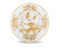 The Oriente Italiano Aurum plate by Ginori 1735 is crafted from white porcelain with scalloped edges and adorned with an intricate gold floral and decorative pattern in the center and around the rim, showcasing the refined elegance of Italian porcelain artistry.