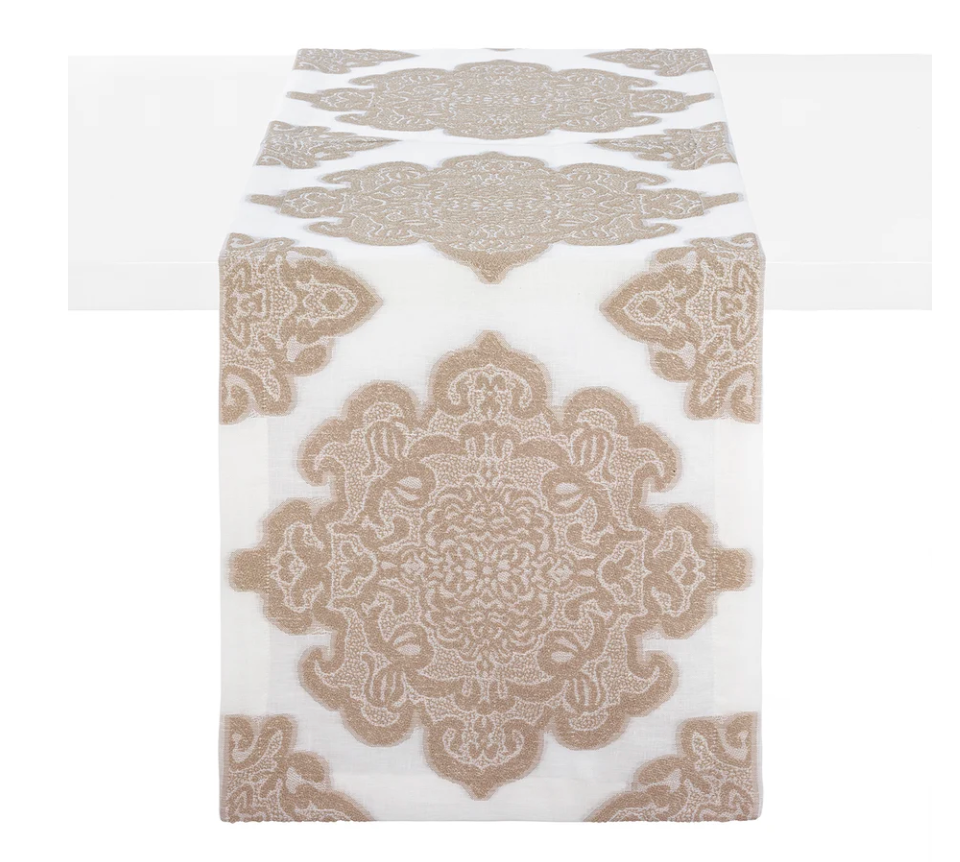 The Castille Table Runner 90″ - Sand by Bodrum features an intricate beige medallion pattern on a white background, elegantly draped over the center of a white table. Part of the refined Castille table linens collection, it is an ideal choice for sophisticated table decor.