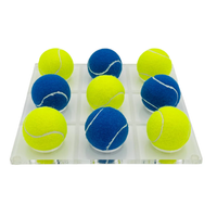 The Tennis Ball Tic Tac Toe - Blue / Yellow by Luxe Dominoes features a 3x3 clear acrylic board with blue and yellow tennis balls—a unique coffee table game and perfect gift for tennis fans.