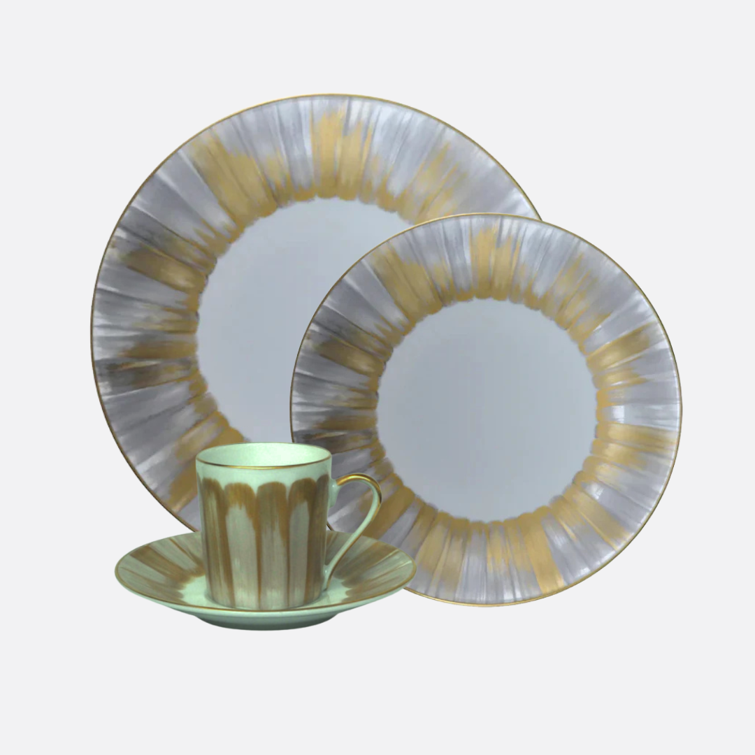 The Marie Daage Panache set by Marie Daâge includes a cup, saucer, and two plates with a radial gold and silver design on white, displayed on a plain grey surface.