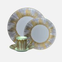 The Marie Daage Panache set by Marie Daâge includes a cup, saucer, and two plates with a radial gold and silver design on white, displayed on a plain grey surface.