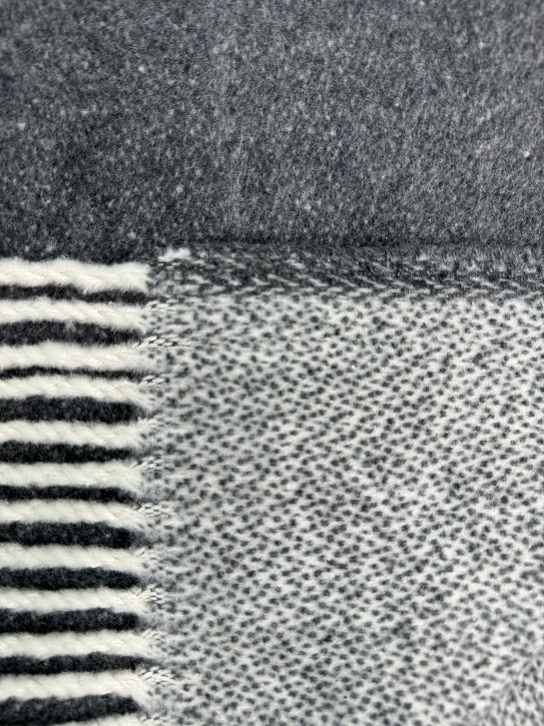 A close-up of the Double Faced Solid Mini Chevron Throw by A Soft Idea, showing gray and white textures with horizontal stripes, a chevron pattern, and bordered by a solid gray section.