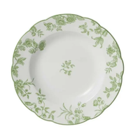 The Albertine Dinnerware by Bernardaud features a round white plate with a scalloped edge, adorned with green floral and leaf patterns around the rim and a delicate central floral motif.