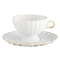 The Vista Alegre 200 Anos Dinnerware features a white ceramic teacup with a gold rim, scalloped gold-edged saucer, and hand-painted trim for modern elegance—an exquisite addition to any luxury table setting.