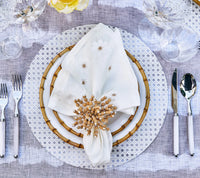 A table setting featuring Kim Seybert's Reed Placemats Set of 4 in White, a decorative plate, bamboo-rimmed plate, beaded ring napkin, glassware, and silver cutlery—yellow flowers complete this chic look for outdoor entertaining.