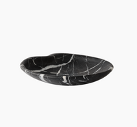 The Lily Marble Bowl Black by Greg Natale features natural black marble with white veining, a shallow rounded shape, and a slight dip on one side, shown against a plain white background.