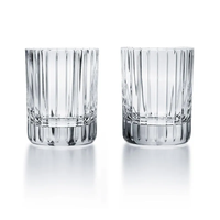 Two clear Baccarat Harmonie highball glasses with vertical ridges stand side by side on a reflective white surface, showcasing the modern design of this Baccarat barware set of 2.