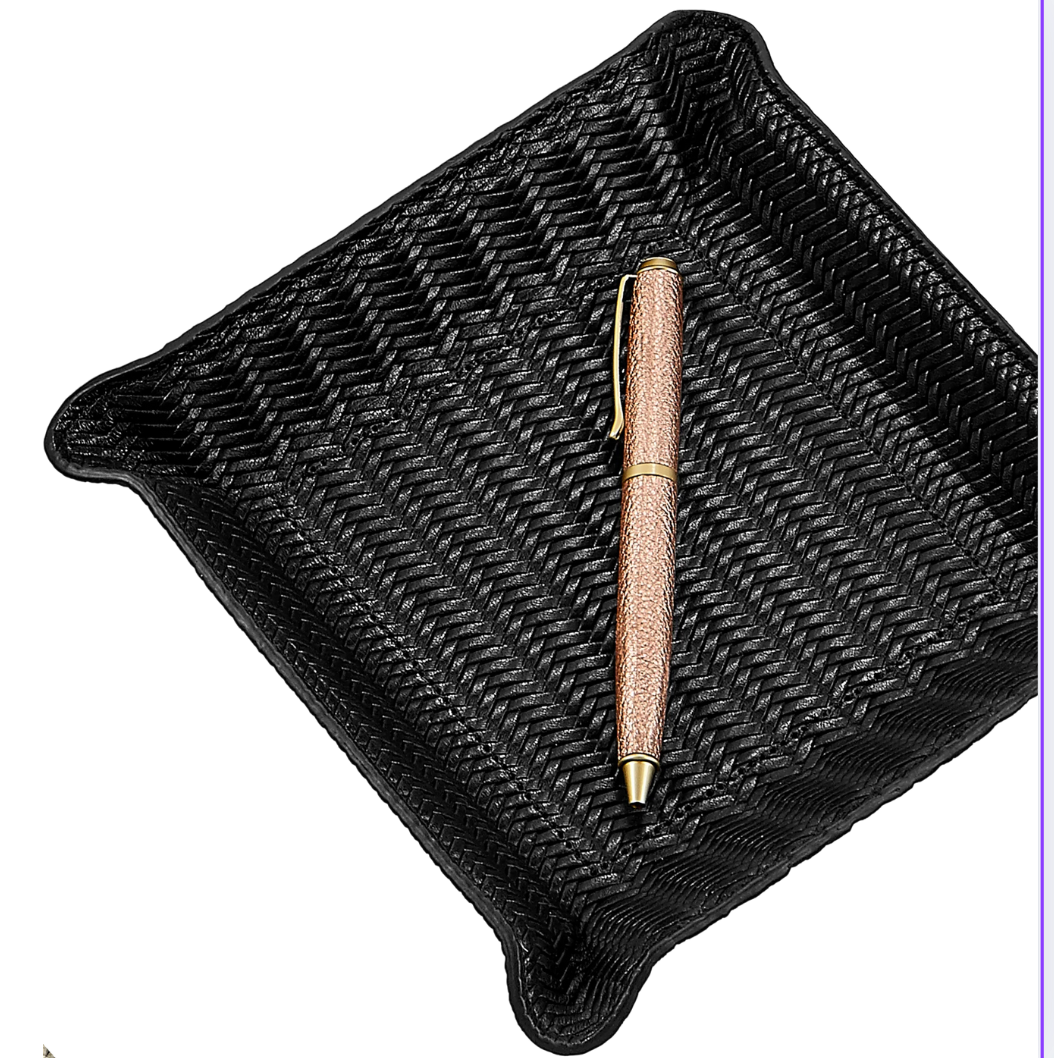 A gold and brown pen rests diagonally inside the Graphic Image Leather Valet Tray - Black Woven, featuring raised corners and a square design, set against a white background.