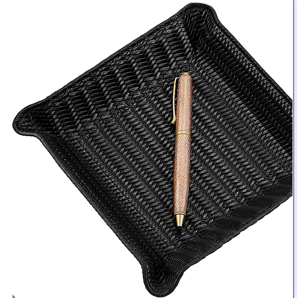A gold and brown pen rests diagonally inside the Graphic Image Leather Valet Tray - Black Woven, featuring raised corners and a square design, set against a white background.