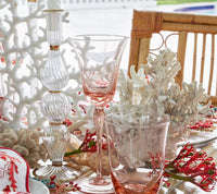Table set with coral decorations, the Kim Seybert Ripple Candle Holder - Clear featuring iridescent luster, two pink-tinted glasses, seashells, and a bamboo chair, creating a coastal and elegant dining atmosphere.