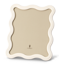 The Ripple Enamel Frame White by L'Objet is a handcrafted Portugal frame with a glossy, wavy border, beige background, modern sculptural design, and the L'Objet logo at the bottom center.