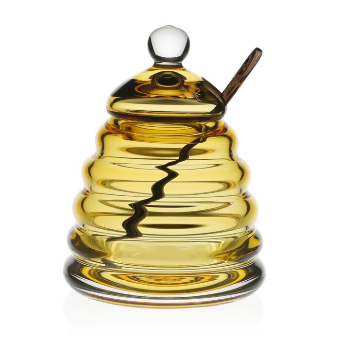 The William Yeoward Honeycomb Jar & Spoon 5" is a golden-yellow glass jar shaped like a bee skep, featuring an amber crystal design, a lid, and side slot for the included wooden spoon—perfect for adding charm to any kitchen.