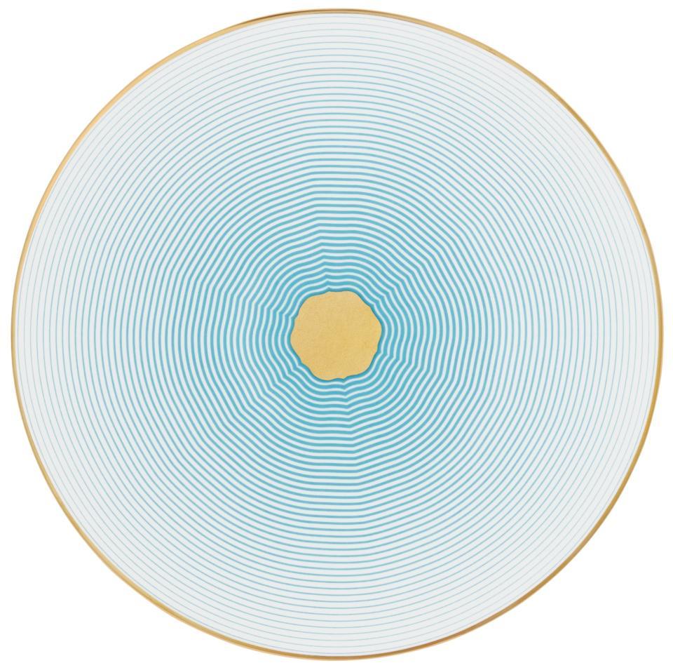 The Aura Dinnerware by Raynaud features a circular plate adorned with concentric turquoise lines radiating from a gold center, fading to white at the edge and finished with a slim gold rim for a modern touch.
