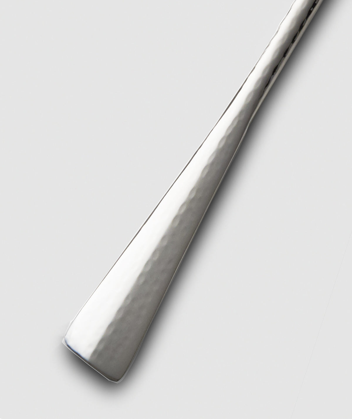 A close-up of the handle of the Mary Jurek Alta Meat Serving Fork, showcasing its hammered stainless steel design, set against a plain light gray background.