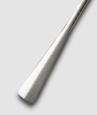 A close-up of the handle of the Mary Jurek Alta Meat Serving Fork, showcasing its hammered stainless steel design, set against a plain light gray background.