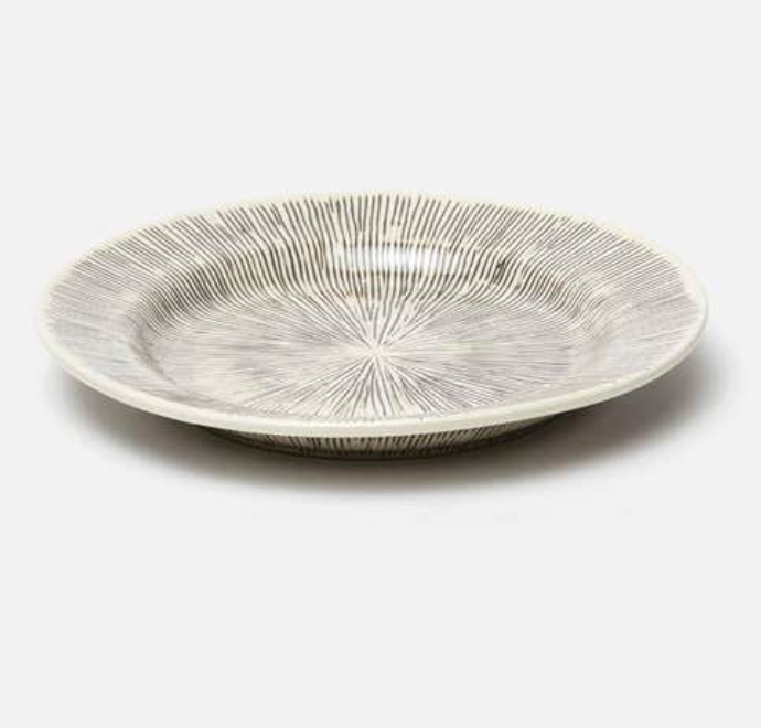 The Nolan Dinnerware Black Cream by Blue Pheasant is a shallow white ceramic bowl with a dark gray radial line pattern, ideal for enhancing your artisanal dinnerware or stoneware collection.