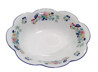 The Nymphea Paradis Bleu bowl by Royal Limoges is a white ceramic piece with scalloped edges, colorful floral patterns, and blue accents around the rim, inspired by classic porcelain design.