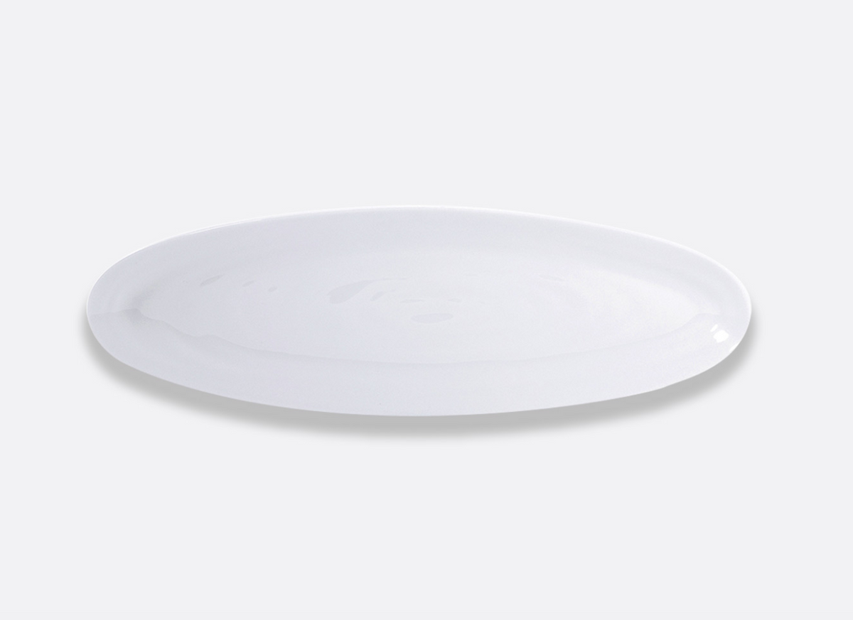 A glossy white oval plate from Bernardaud Origine Dinnerware is centered on a light gray background.